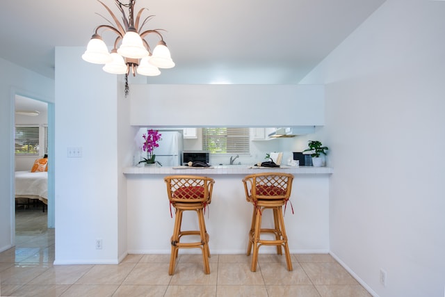 kitchen featuring a kitchen breakfast bar, a notable chandelier, kitchen peninsula, white fridge, and pendant lighting