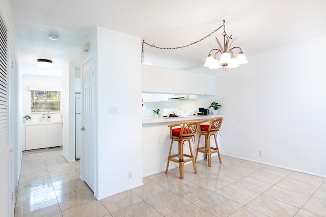 kitchen with kitchen peninsula, a kitchen breakfast bar, pendant lighting, a notable chandelier, and white cabinets