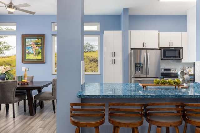 kitchen with appliances with stainless steel finishes, backsplash, light hardwood / wood-style floors, white cabinetry, and ceiling fan