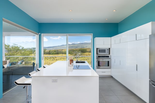 kitchen featuring appliances with stainless steel finishes, sink, tile patterned floors, an island with sink, and white cabinetry