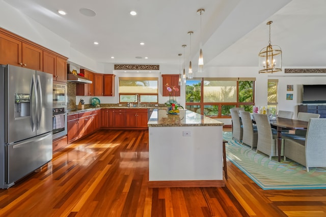 kitchen with wall chimney range hood, dark wood-type flooring, decorative light fixtures, and appliances with stainless steel finishes