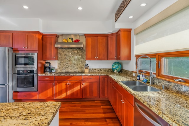 kitchen with light stone counters, dark hardwood / wood-style flooring, wall chimney range hood, appliances with stainless steel finishes, and sink