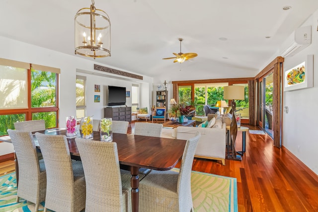 dining space with vaulted ceiling, hardwood / wood-style floors, a wall unit AC, and ceiling fan with notable chandelier