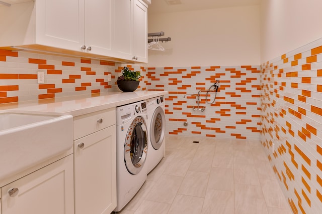 clothes washing area featuring washing machine and clothes dryer, light tile patterned floors, and cabinets