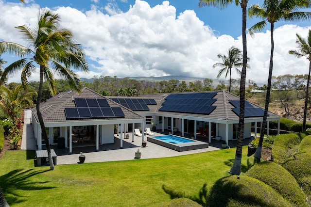 rear view of house with a lawn, a pool with hot tub, solar panels, and a patio