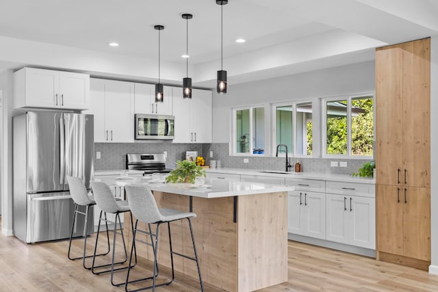 kitchen featuring appliances with stainless steel finishes, white cabinets, decorative light fixtures, and a kitchen island