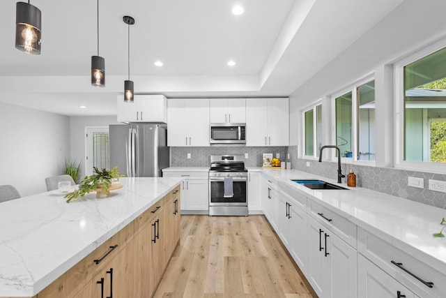 kitchen featuring sink, hanging light fixtures, white cabinetry, stainless steel appliances, and light stone counters