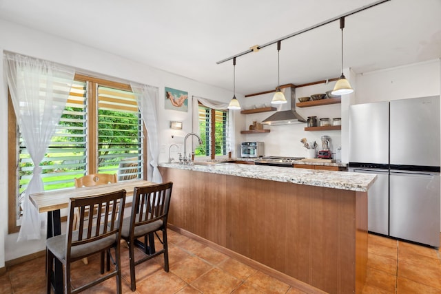 kitchen featuring kitchen peninsula, light stone counters, stainless steel appliances, sink, and decorative light fixtures