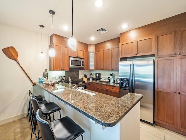 kitchen with sink, stainless steel appliances, kitchen peninsula, pendant lighting, and a kitchen bar