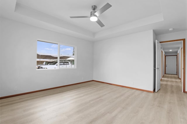 unfurnished room with light wood-type flooring, a raised ceiling, and ceiling fan