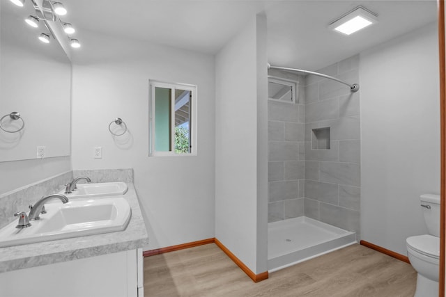 bathroom with tiled shower, vanity, wood-type flooring, and toilet