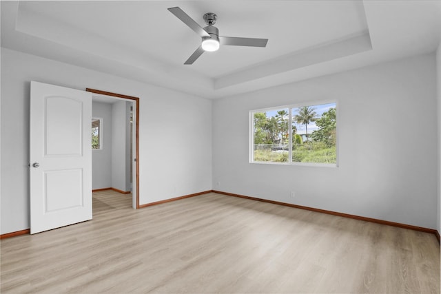 unfurnished room featuring a raised ceiling, ceiling fan, plenty of natural light, and light wood-type flooring