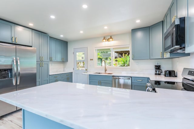 kitchen with appliances with stainless steel finishes, sink, light stone counters, kitchen peninsula, and light hardwood / wood-style flooring