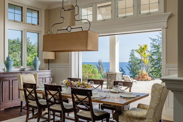 dining space with a water view, a wainscoted wall, a healthy amount of sunlight, and a decorative wall