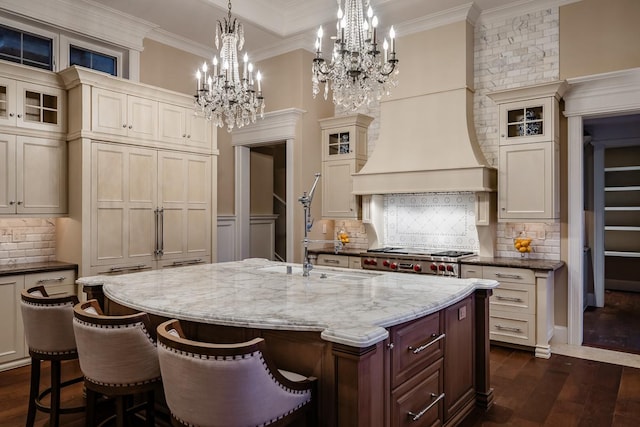 kitchen featuring glass insert cabinets, cream cabinetry, a kitchen island with sink, and custom exhaust hood