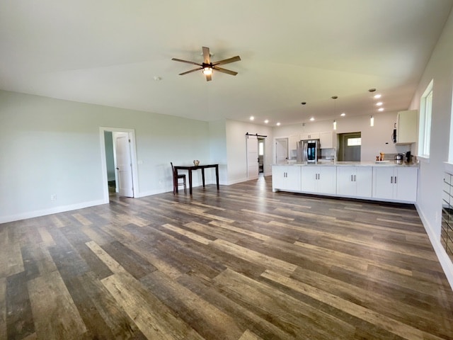 unfurnished living room with ceiling fan, a barn door, and dark hardwood / wood-style flooring