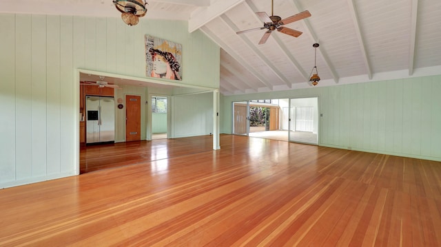 unfurnished living room featuring vaulted ceiling with beams, ceiling fan, wooden walls, and wood-type flooring