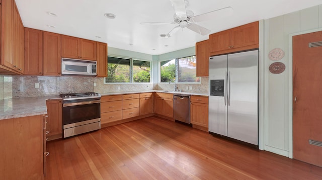 kitchen featuring ceiling fan, sink, light stone counters, light hardwood / wood-style flooring, and appliances with stainless steel finishes