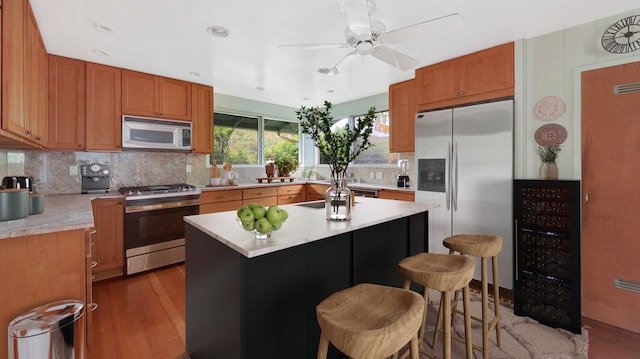 kitchen featuring wood-type flooring, a kitchen bar, decorative backsplash, a kitchen island, and appliances with stainless steel finishes