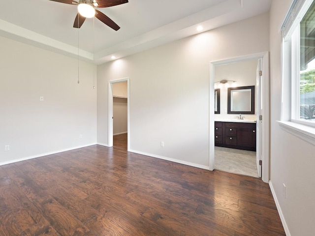 unfurnished bedroom featuring a spacious closet, ceiling fan, ensuite bathroom, and dark wood-type flooring