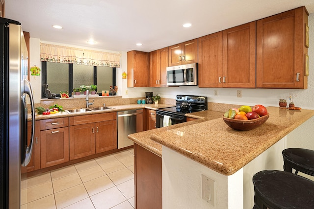 kitchen featuring stainless steel appliances, sink, light stone counters, a kitchen bar, and kitchen peninsula