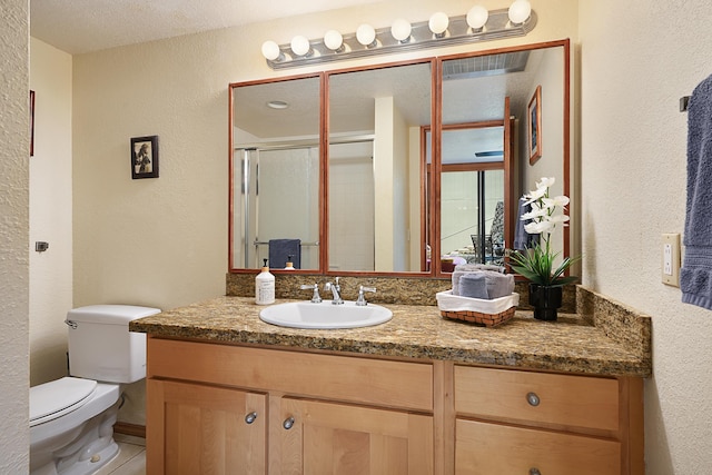 bathroom featuring a textured ceiling, an enclosed shower, vanity, and toilet