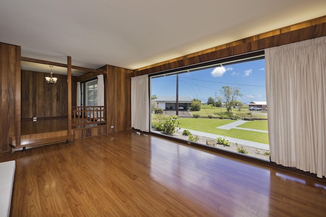 spare room featuring hardwood / wood-style flooring, a notable chandelier, and wooden walls