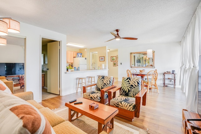 living room featuring a textured ceiling, light wood-type flooring, ceiling fan, and sink