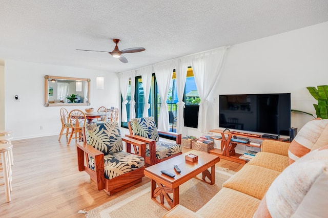 living room with ceiling fan, light wood-type flooring, and a textured ceiling