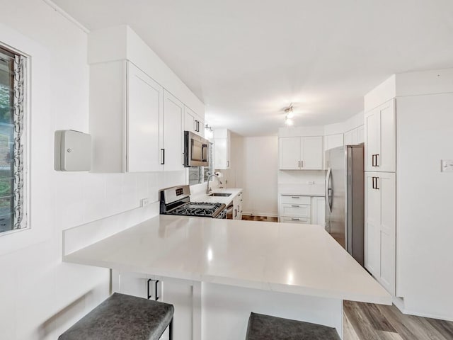 kitchen featuring kitchen peninsula, appliances with stainless steel finishes, a kitchen bar, sink, and white cabinets