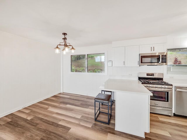 kitchen with light hardwood / wood-style floors, a kitchen bar, hanging light fixtures, and appliances with stainless steel finishes