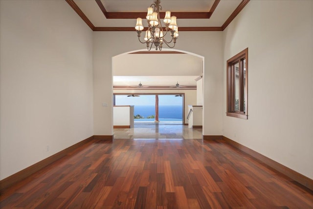 spare room with dark wood-type flooring, crown molding, a notable chandelier, and a water view