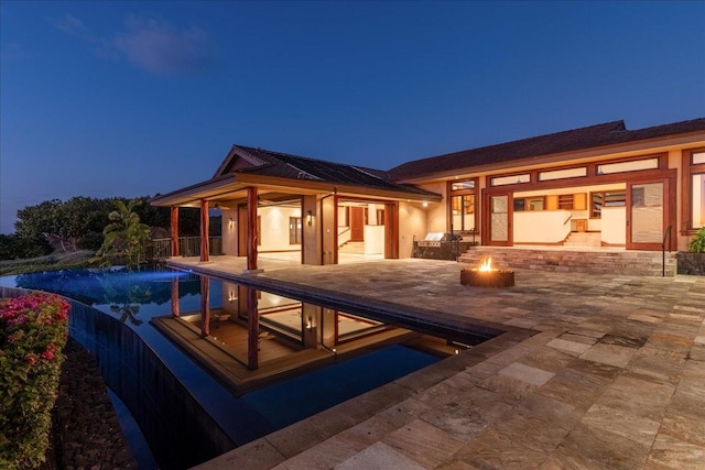 back house at dusk featuring a fire pit, solar panels, a patio, and pool water feature