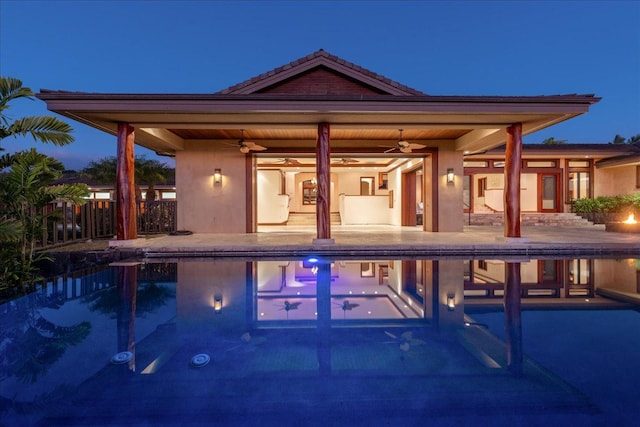 pool at dusk featuring ceiling fan and a patio