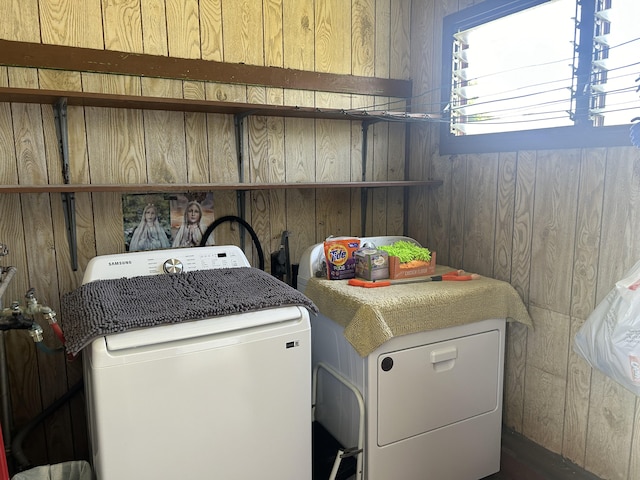 clothes washing area featuring independent washer and dryer and wood walls