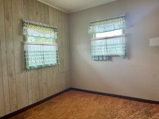 carpeted spare room featuring baseboards, wooden walls, and ornamental molding