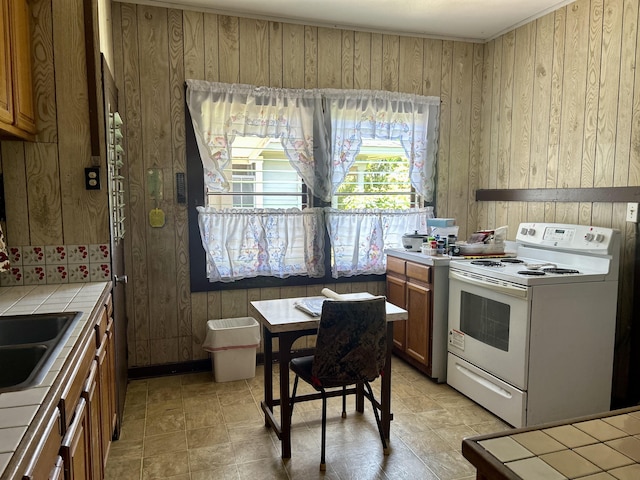 kitchen with brown cabinetry, baseboards, electric range, a sink, and tile counters