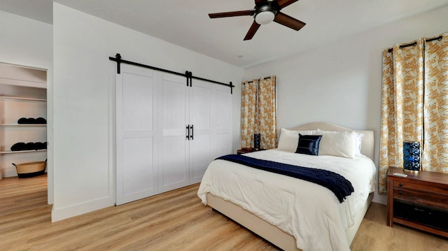 bedroom with a barn door, light hardwood / wood-style floors, and ceiling fan