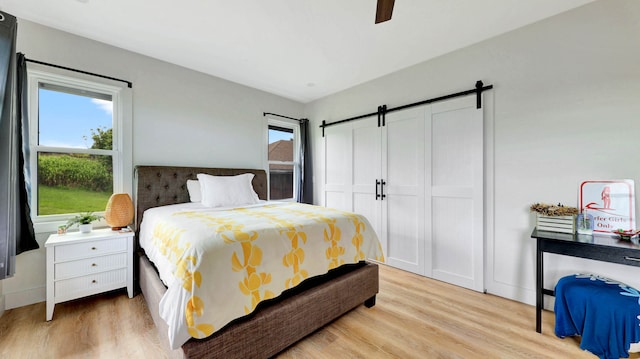 bedroom with a barn door, ceiling fan, and light hardwood / wood-style floors