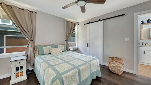 bedroom with ensuite bathroom, ceiling fan, a barn door, dark wood-type flooring, and sink