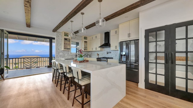 kitchen featuring stainless steel fridge with ice dispenser, light hardwood / wood-style flooring, wall chimney exhaust hood, beam ceiling, and backsplash