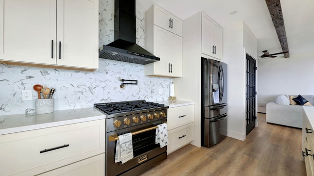 kitchen featuring hardwood / wood-style flooring, tasteful backsplash, wall chimney exhaust hood, white cabinets, and appliances with stainless steel finishes