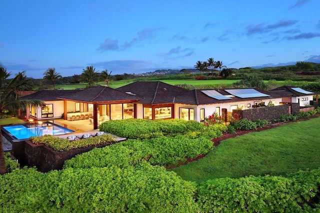 back house at dusk featuring a lawn and solar panels