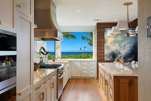 kitchen with sink, pendant lighting, light wood-type flooring, custom exhaust hood, and high end stove