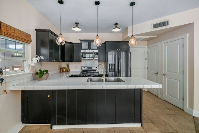 kitchen featuring kitchen peninsula, appliances with stainless steel finishes, sink, light tile patterned floors, and pendant lighting