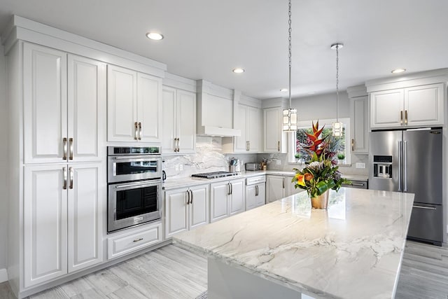 kitchen with white cabinetry, light stone countertops, hanging light fixtures, stainless steel appliances, and a kitchen island