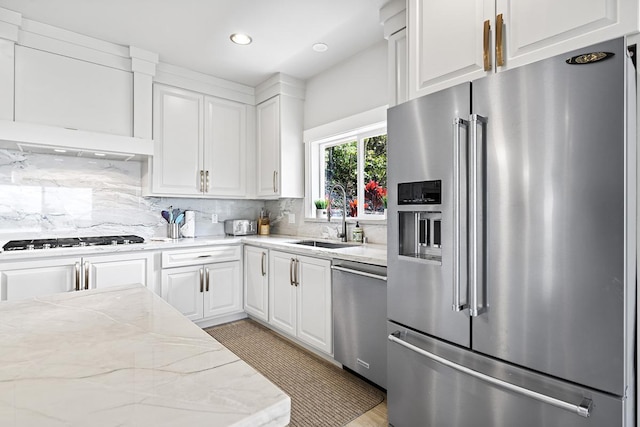 kitchen featuring light stone countertops, backsplash, stainless steel appliances, sink, and white cabinets