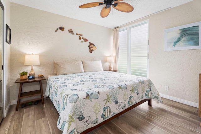 bedroom with a textured ceiling, ceiling fan, multiple windows, and hardwood / wood-style floors