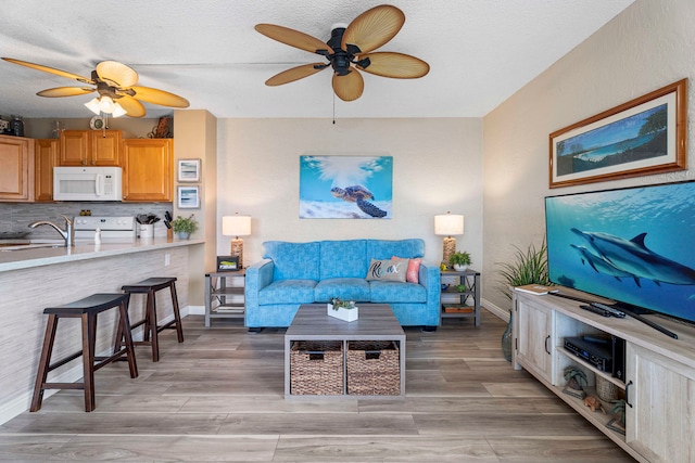 living room featuring ceiling fan, light hardwood / wood-style flooring, and sink