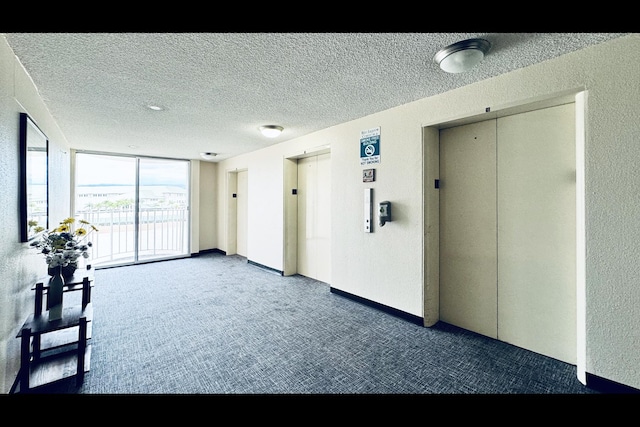 interior space featuring a textured ceiling, dark carpet, floor to ceiling windows, and elevator